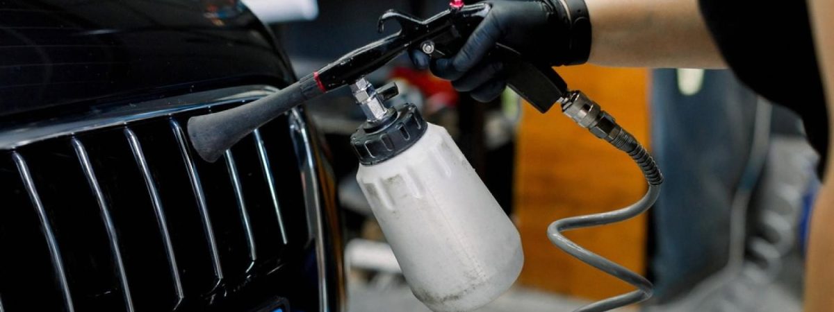 Detailer using a spray gun to apply paint sealant on a black car